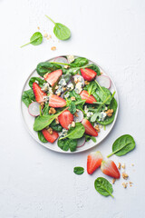 Summer, fresh salad with leafy greens, fresh strawberries, nuts, radishes  and farm cheese on a white background. Healthy summertime food concept
