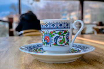 Traditional turkish coffee pot and dish with iznik tile gravures on the cup in cafe and wooden table.