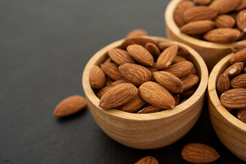 Wooden bowl with almond on black background. Top view. Flat lay (selective focus; close-up shot)