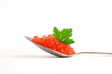 Silver spoon with red caviar and green parsley leaf on top isolated on white background. Close up.