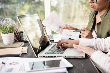 Side view of businesswoman's hands using laptop computer placed on messy office desktop. teamwork with business people analysis cost graph on desk at meeting room.