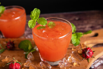 Iced roselle tea glass with fresh roselle fruit on wooden table for healthy herbal drink concept. herbal organic tea for good healthy.