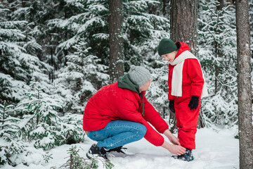 Fototapeta na wymiar A caring father adjusts his son's winter suit during a walk in the park in winter