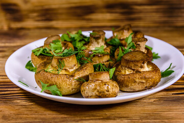 Plate with baked champignons, dill and parsley on a wooden table