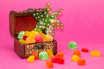 Chest with gummies and windmill on pink background