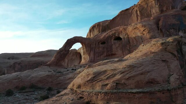 Large red rock arch in the desert at dusk. Aerial 4K drone video flying slow and low over rocks.