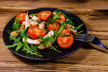 Roasted chicken breasts and salad with arugula and cherry tomatoes in a black plate