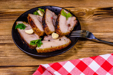 Slices of baked pork belly, garlic and parsley on a black plate