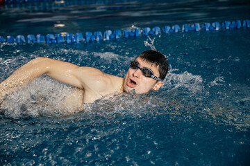 Caucasian athlete-swimmer crawls in the blue water. Portrait of a young male triathlete swimming in swimming goggles. Triathlon training concepts for triathletes