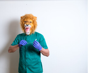 Doctor in an angry lion mask with a syringe in hands standing near a white wall