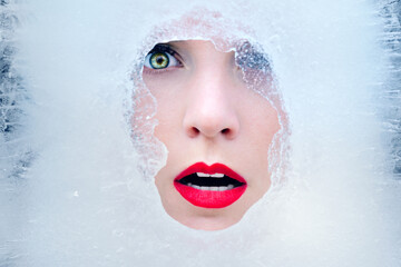 Beautiful young woman face in ice. Frozen winter beauty with red lips in ice cube. Fashion art woman portrait.