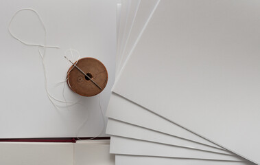 folded paper signatures, wooden spindle with white nylon thread, and needle - bookbinding theme