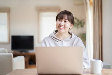 リビングで笑顔でパソコン操作をするアジア人女性