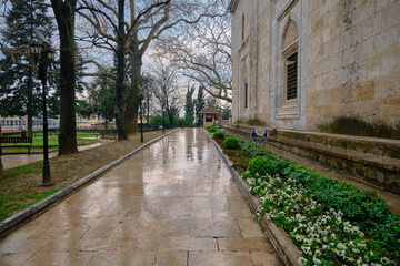 Rainy day in Bursa in Green mosque (yesil cami) and way covered by green grass made of marble and reflection of trees on puddle existing on the walking path near the mosque.