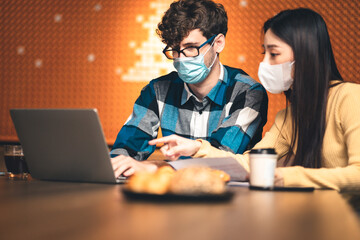 young asian woman and caucasian man Business people Working discuss finding new strategy solution.People putting  protective face mask discussion business plan using laptop at cafe.