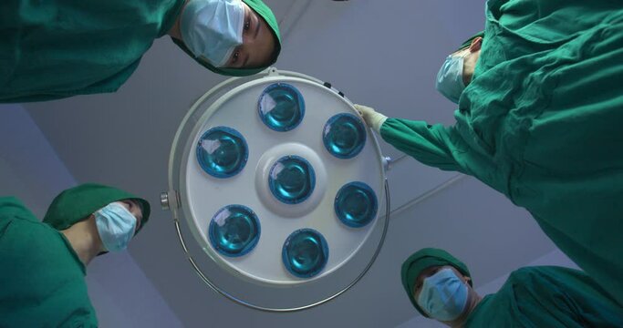 POV Group of asian doctors wearing full surgical scrubs looking at the patient in operating theater at the hospital. Teamwork, Healthcare and medical technology concept.