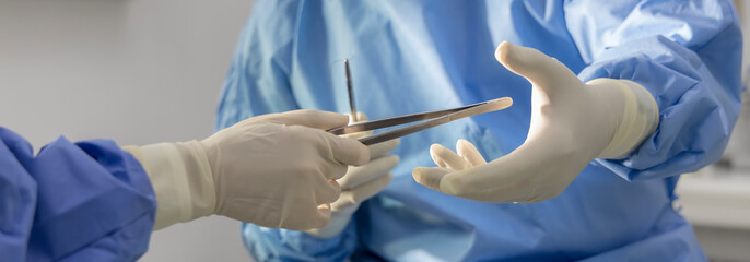Close up photo of surgeon 's hand with forceps.Doctor in blue surgical gown suite make the surgery...
