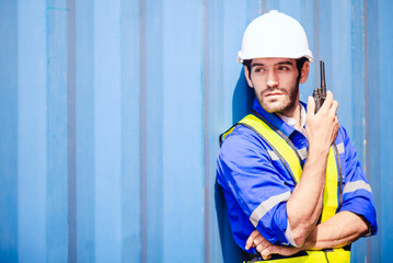 Portrait of man engineer or worker holding walkie talkie wears white hardhat and reflecting cloth with cargo container background and copy space. Concept engineering site communication.