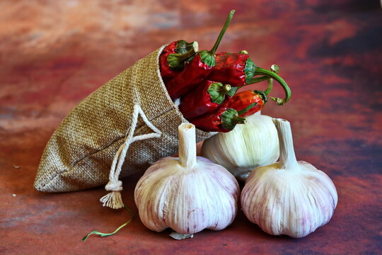 canvas bag with bunch of red hot chili peppers on three garlic bulbs on brown background
