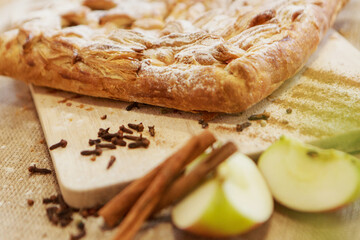Pie, apples, and cinnamon on a chopping board. The food is ready to eat. Puff pastry