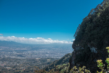 View from the lookout point towards the capital city of San José, Costa Rica and a stone wall covered in vegetation in the middle of a sunny summer day