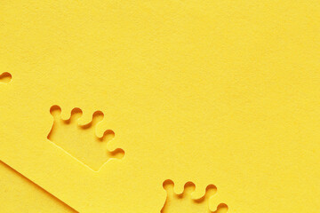 perforated crown on yellow background, paper texture with crown shaped hole, top view with copy space on the right, flatlay colored light paper