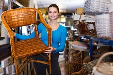 happy young customer woman standing with wicker chair in shop for decor