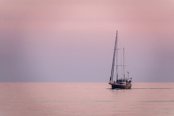 Sailing yacht in the blue sea during beautiful pink sunset.