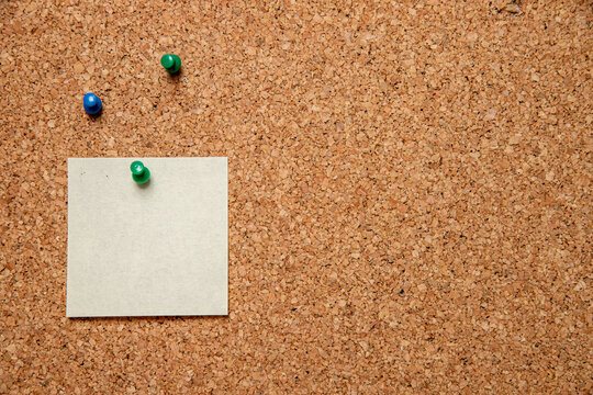 Closeup shot of three pins and an empty white paper with space for text on a corkboard
