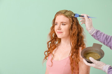 Dyeing hair of young woman with henna on color background