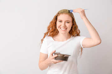 Young woman using henna hair dye on light background