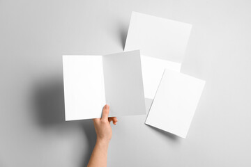 Hand with blank brochures on light background