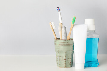 Holder with different tooth brushes, paste and rinse on light background