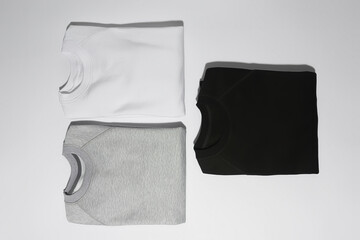 Flat lay of three perfectly folded monochrome sweatshirts gray, black and white isolated over white...