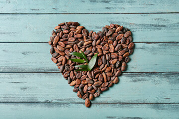 Heart made of cocoa beans on color wooden background