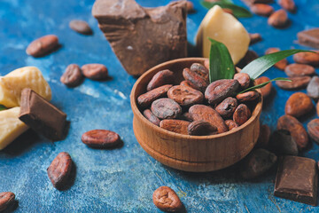 Bowl with cocoa beans on color background