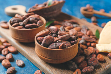 Bowls with cocoa beans on color background