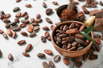 Bowl with cocoa beans on light background