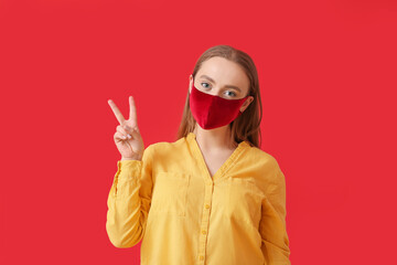 Stylish young woman wearing mask and showing victory gesture on color background