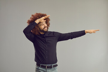 Let's party. Happy funny young man with crazy hair style dancing and having fun in studio. Goofy carefree guy wearing curly brown wig doing dab dancing move isolated on gray background