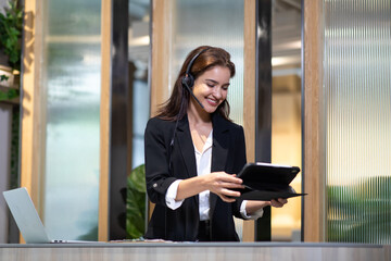 Attractive business woman Asian in suits and headsets are smiling while working with computer at office. Customer service assistant working in office. VOIP Helpdesk headset