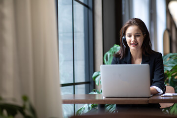 Attractive business woman Asian in suits and headsets are smiling while working with computer at...
