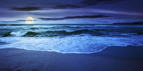 sea tide on a cloudy sunrise. green waves crashing golden sandy beach in full moon light. storm...