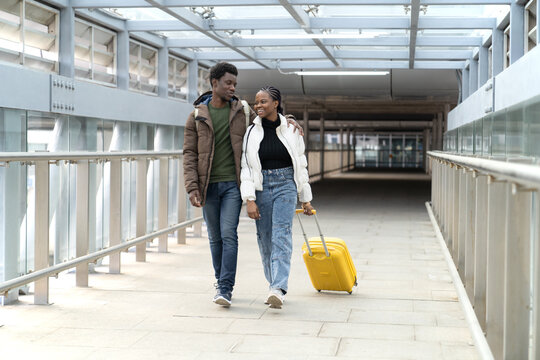 Smiling african couple in airport walk for boarding with suitcase travel after end covid-19 lockdown. Happy couple of travelers before departure to vacation trip after vaccine and new travel normality