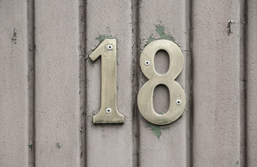 18 eight-teen house number plate hanged on a concrete fence. Arhitectural detail.