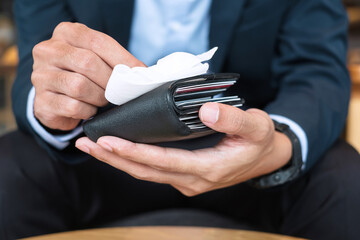 Businessman in suit cleaning money wallet by wet wipes tissue and alcohol disinfectant at office or cafe, protection coronavirus (Covid-19) infection. New Normal and Clean surface concept