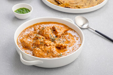 butter chicken, an Indian creamy chicken gravy served in a white bowl with roti or naan