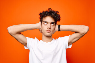 guy in a white t-shirt with curly hair holding his head emotions orange background