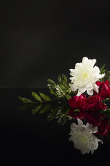 Beautiful bouquet of flowers: red roses, white chrysanthemums, green leaves on black background