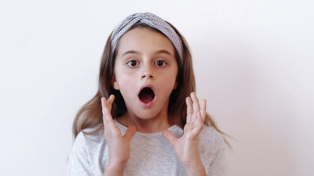 Shocked kid. Fear horror. Disturbing news. Panic attack. Astounded terrified scared small girl covering open mouth with hands showing omg reaction isolated on light neutral empty space background.